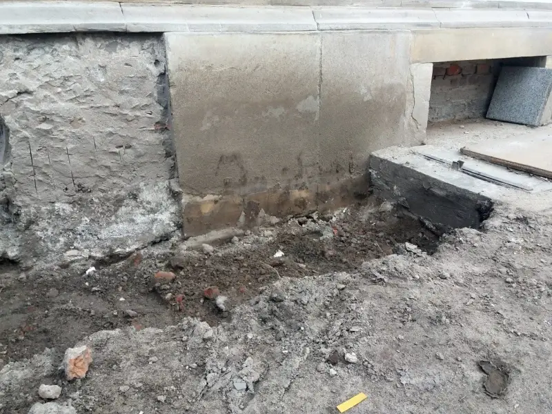 Odsłonięty fundament z cegły, ziemia i gruz wokół. Trwa remont.