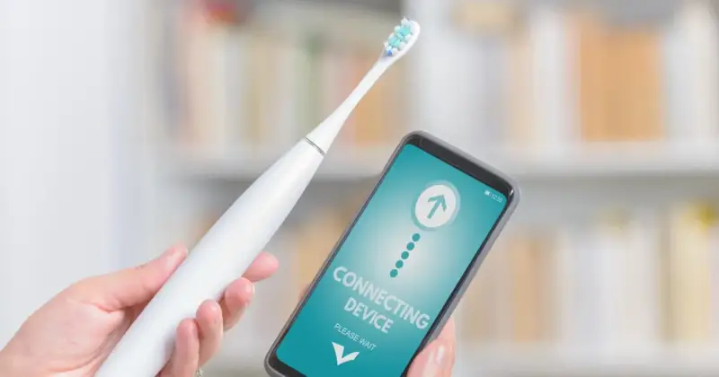 Ręka trzyma białą szczoteczkę elektryczną i smartfon z napisem "CONNECTING DEVICE". Czy mogę wziac szczoteczke elektryczna do samolotu?