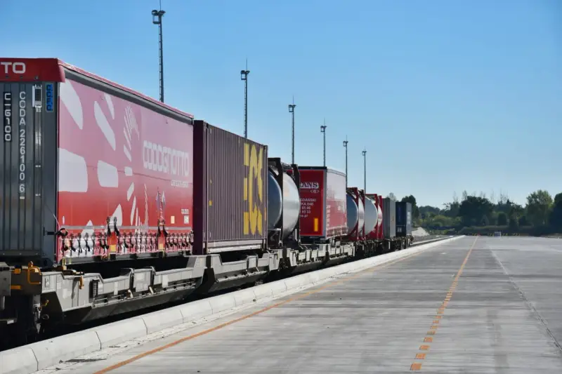 Długi pociąg towarowy z kontenerami, w tym czerwonymi z logo COSCO i żółtymi, czeka na dalszy transport kolejowy.