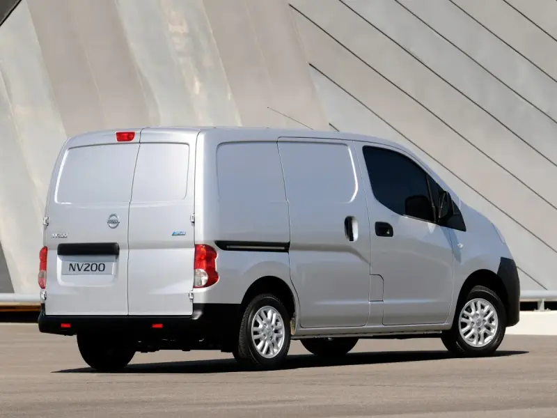 Srebrny Nissan NV200, wszechstronny van, zaparkowany przed nowoczesnym budynkiem.