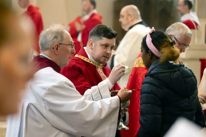 Clergy in red robes perform communion, a sacred act that can be seen as a form of evangelizing, sharing faith with a young woman.