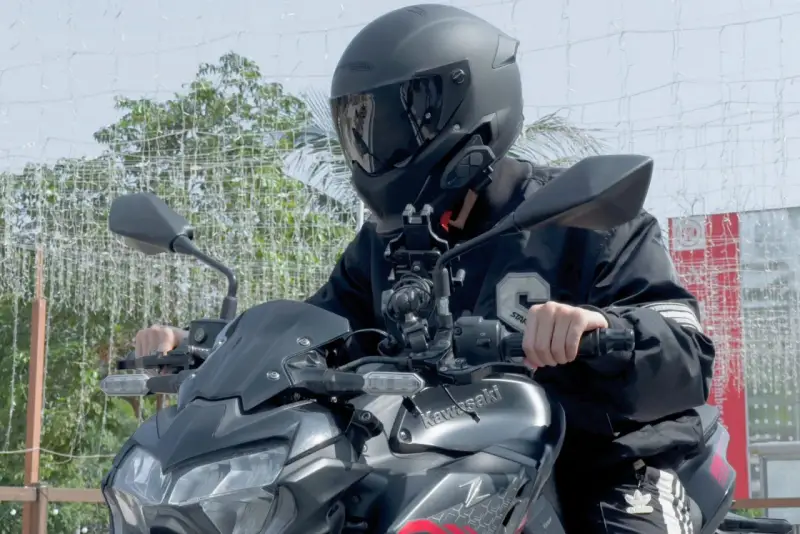 Motocyklista w kasku siedzi na motocyklu Kawasaki, z zamontowanym interkomem na kasku.