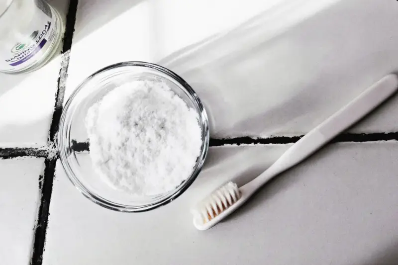 Bicarbonate de soude dans un bol et une brosse à dents sur un carrelage.