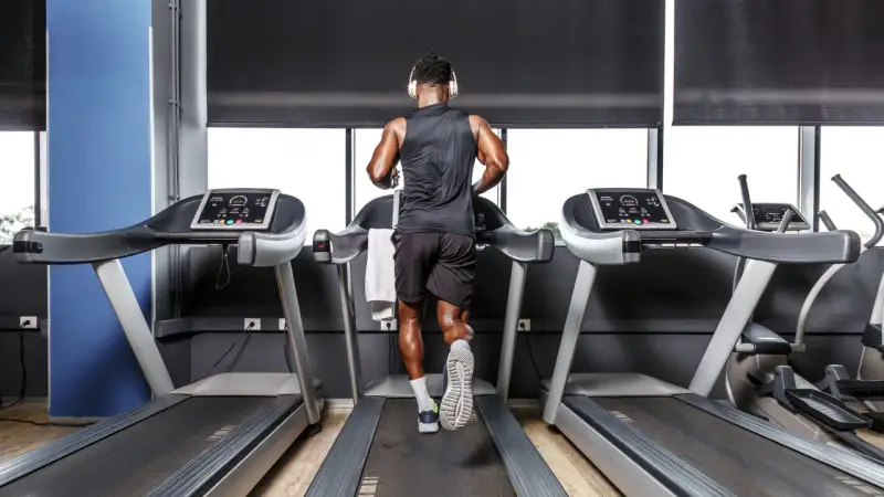 Mann mit Kopfhörern absolviert ein intensives Laufband Training in einem modernen Fitnessstudio.