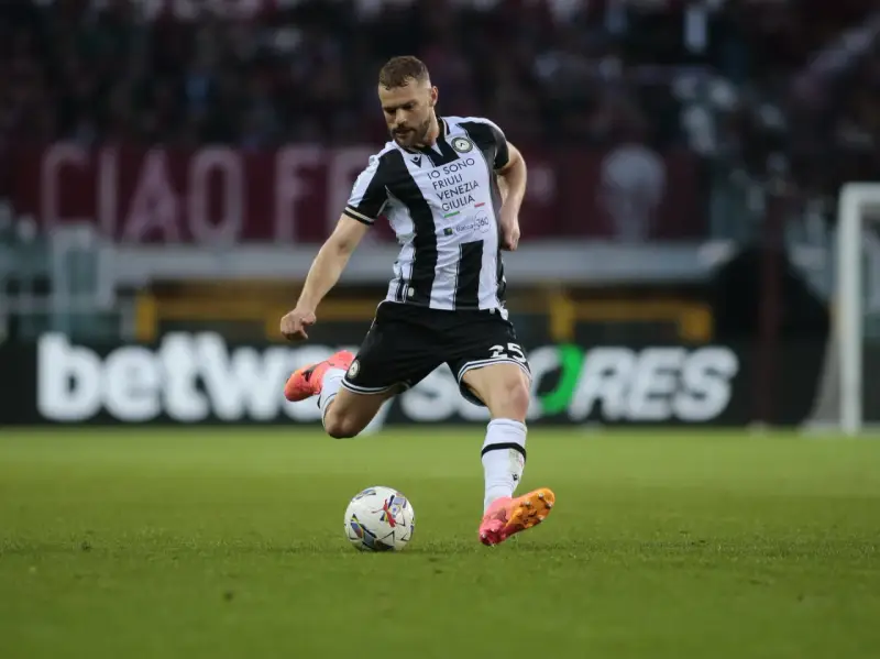 Piłkarz Jesper Karlström w czarno-białej koszulce Udinese Calcio kopie piłkę na zielonej murawie stadionu.