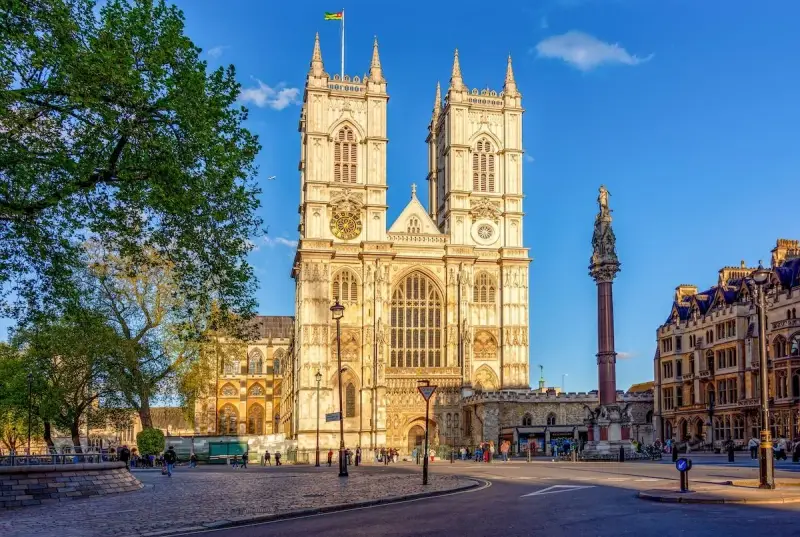 L'abbaye de Westminster, majestueuse et illuminée par le soleil, se dresse fièrement avec ses tours jumelles. Une colonne commémorative se dresse à droite.