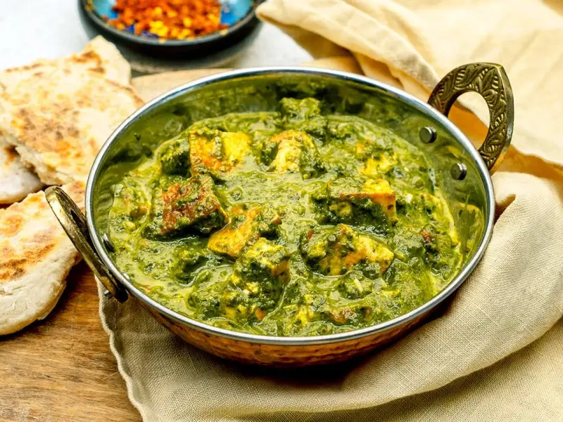 Ein köstliches Palak Paneer in einer traditionellen Schüssel, serviert mit Fladenbrot und Gewürzen.