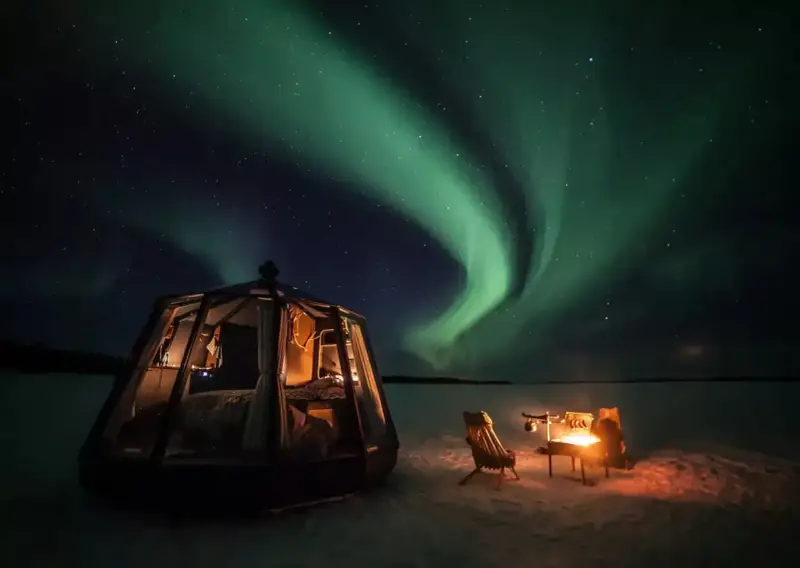 Drömmen att bo i igloo och se norrsken blir verklighet. En glaskupol med säng och en mysig eldstad utomhus under en magisk himmel.