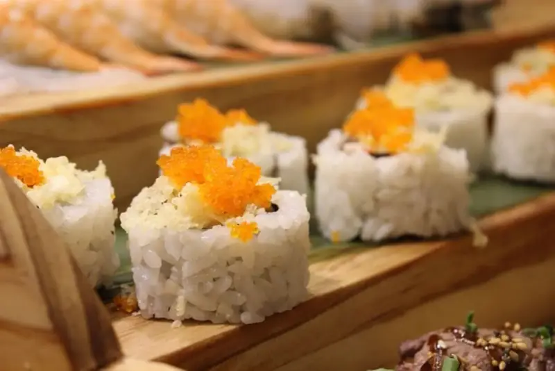 Roladki sushi z pomarańczową ikrą i chrupiącą posypką, idealne do słodkiego sosu do sushi.