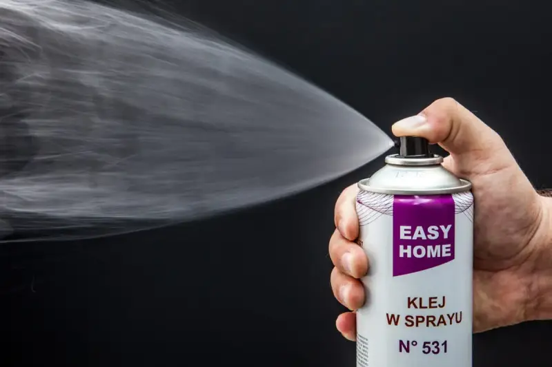 Dłoń trzyma puszkę z klejem w sprayu, który jest rozpylany. Idealny klej do podsufitki bez zdejmowania.