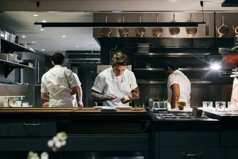 Chefs in a professional kitchen, one plating food.