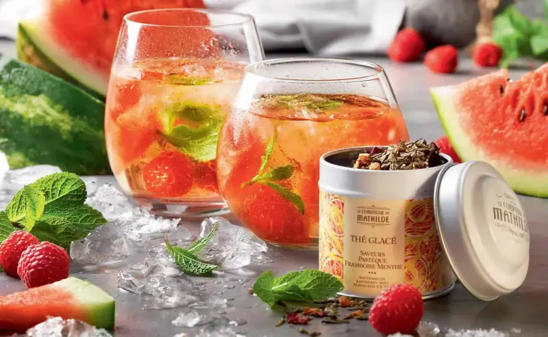 Rafraîchissante recette thé glacé : deux verres remplis de glaçons, fruits rouges et menthe, accompagnés de pastèque et d'une boîte de thé.