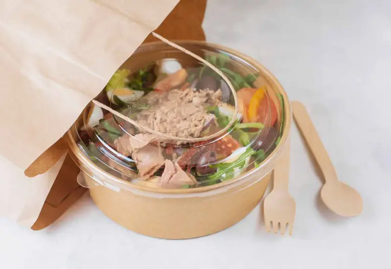 Ensalada de atún para llevar, con ingredientes frescos y cubiertos en un recipiente ecológico. Perfecta para tu licencia take away.