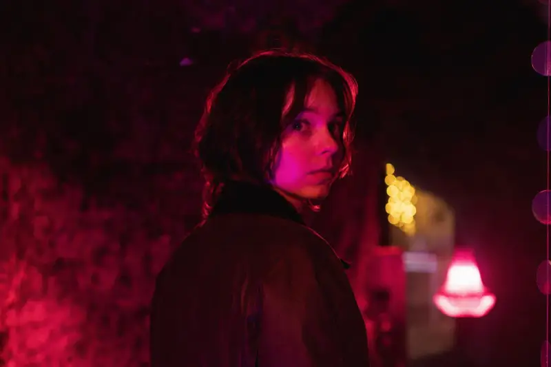 Młoda kobieta z zaciekawieniem spogląda przez ramię w mrocznym, neonowym otoczeniu. Czy to scena z nowego serialu Netflix?
