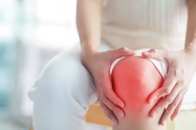 Hände umfassen ein schmerzendes Knie, das rot aufleuchtet, ein Zeichen für Arthrose im Knie.
