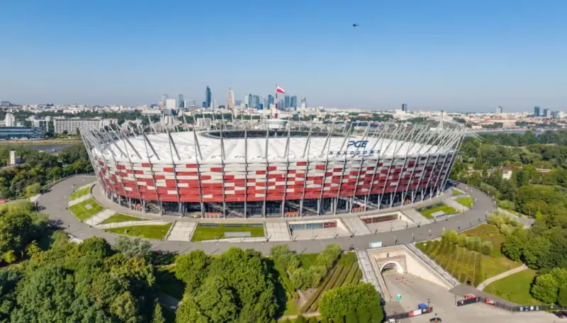 PGE Narodowy, jeden z największych stadionów w Polsce, w otoczeniu zieleni i warszawskiej panoramy.
