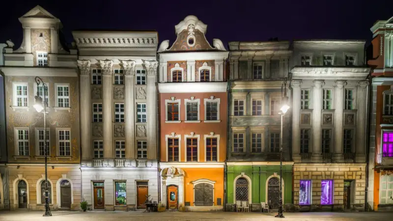 Nocny widok na kolorowe kamienice Starego Rynku w Poznaniu, przypominające urokliwe osiedle warszawskie.