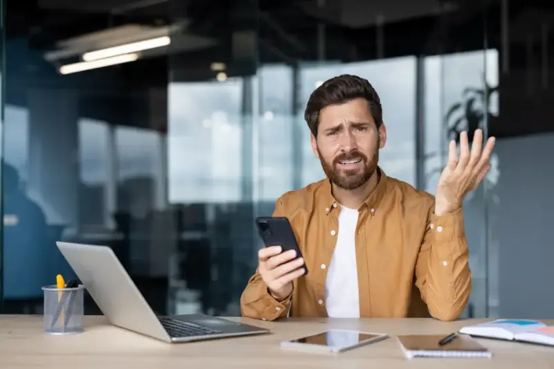 Zdezorientowany mężczyzna trzyma telefon, jakby właśnie dowiedział się o problemach z cesją.