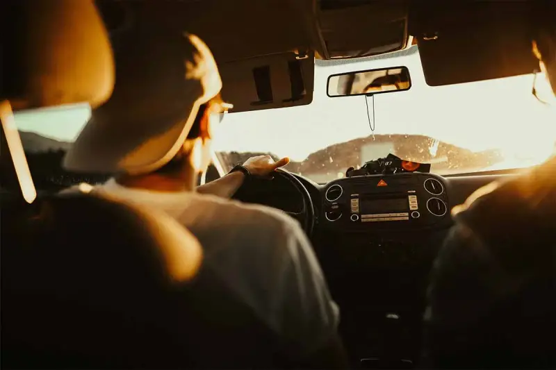 Hombre con gorra al volante, listo para planificar viaje en coche. El sol ilumina el interior del vehículo.