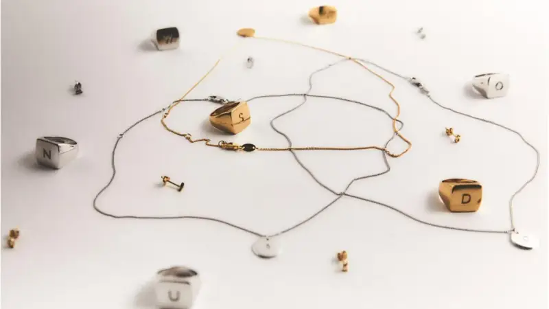 Joyas con letras, como limpiar la plata para que brillen. Anillos y collares dorados y plateados sobre fondo blanco.