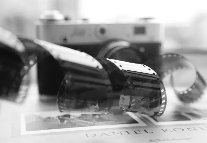 Analogowa fotografia: zwoje kliszy filmowej przed aparatem, na tle książki z napisem "DANIEL KONI".
