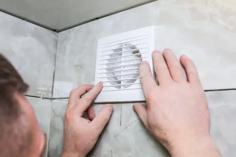Mains d'homme ajustant une grille de VMC dans une salle de bain car une mauvaise odeur persiste.