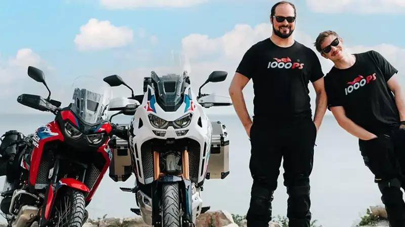 Dwóch mężczyzn w koszulkach 1000PS obok motocykli Honda Africa Twin.