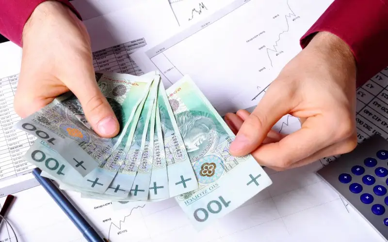 Ręce trzymające polskie stuzłotówki, obok kalkulator i wykresy. Jak wypłacić pieniądze z PPK?