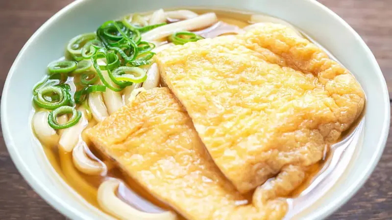 Pyszna zupa z makaronem udon z dwoma kawałkami smażonego tofu i zieloną cebulką.