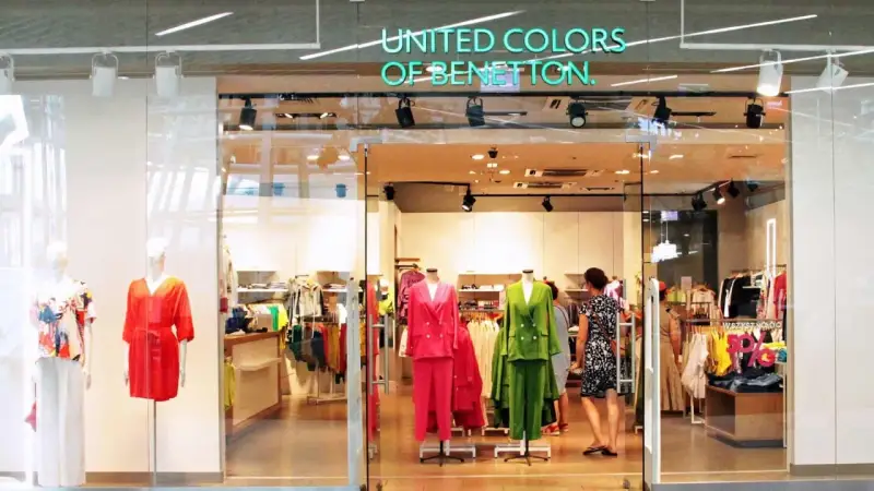 Witryna sklepu United Colors of Bennetton z kolorowymi ubraniami na manekinach i wieszakach.