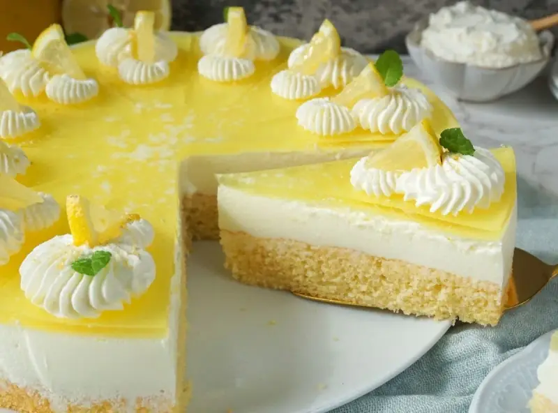 Erfrischende joghurt-torte mit biskuitboden, dekoriert mit Zitronenspalten und Sahnetupfern.