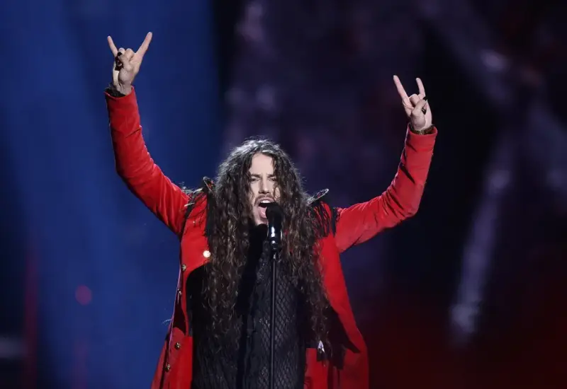 Michał Szpak na Eurowizji w czerwonej marynarce, z uniesionymi rękami i gestem rock'n'rolla.