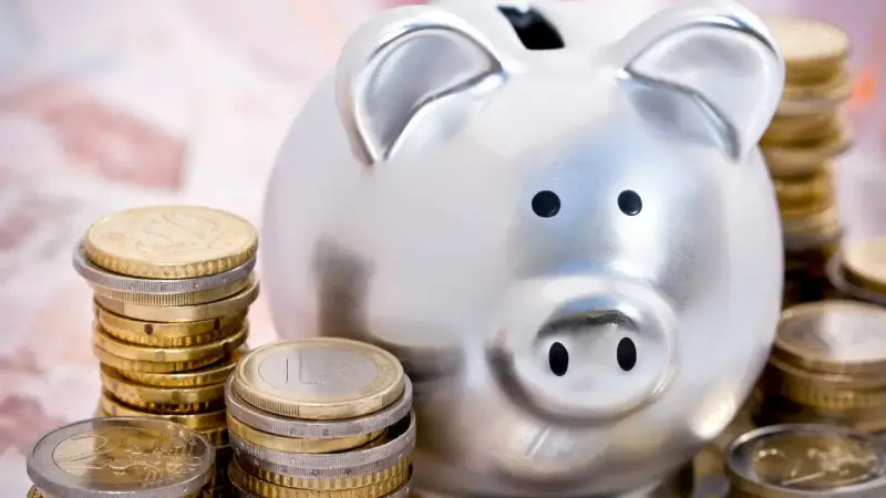 Hucha plateada rodeada de pilas de monedas de euro, simbolizando las ventajas del euro para el ahorro.