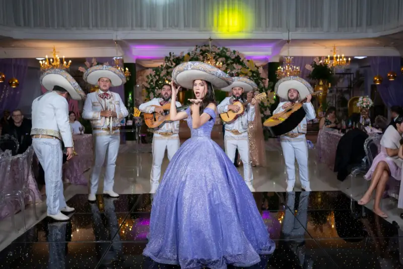 Mariachi grają, a dziewczyna w fioletowej sukni posyła całusy. W tle weselne dekoracje i goście. Idealna sceneria do przyśpiewki weselne tekst.