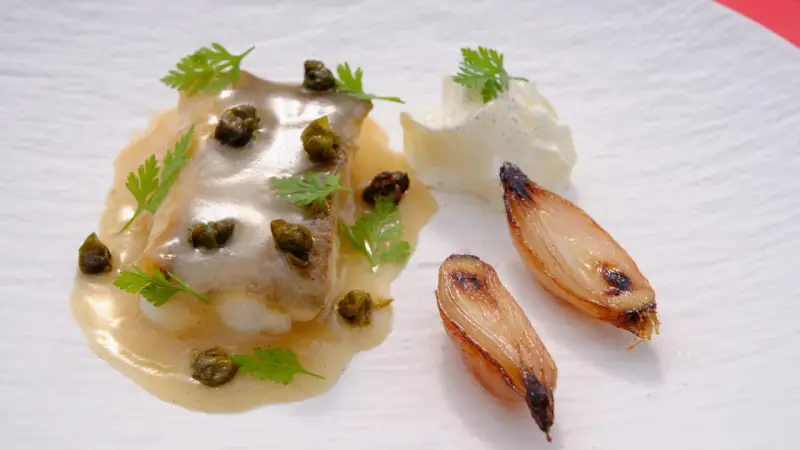 Delicioso lenguado a la meunière con alcaparras, perejil, cebollas caramelizadas y una quenelle de crema.