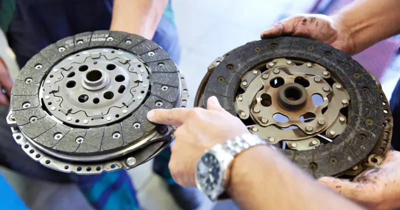 Mechanik pokazuje dwa dyski sprzęgła: jeden nowy, drugi mocno zużyty, z widocznymi śladami spalonego sprzęgła.