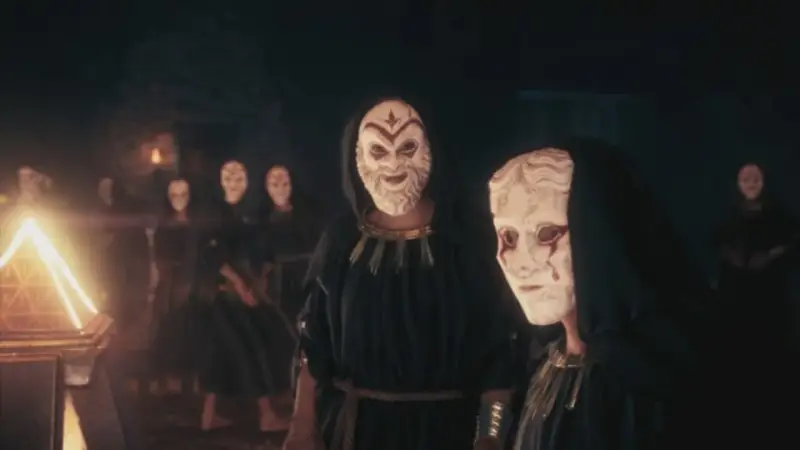 Miembros del culto de Kosmos, con túnicas oscuras y máscaras blancas, se reúnen ante un objeto piramidal brillante.