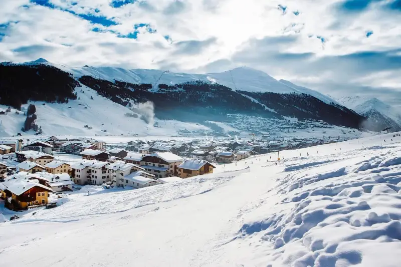 Paesaggio invernale con villaggio innevato e montagne sullo sfondo. Perfetto per sapere dove andare in montagna in Trentino per sciare.