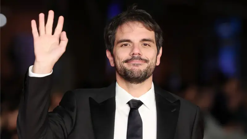 Valerio Vestoso saluta con la mano, sorridendo con un abito elegante.