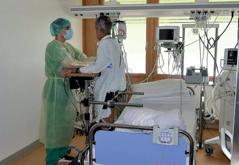 Pflegekraft unterstützt Patientin bei der Reha nach Intensivstation. Sie üben das Aufstehen.