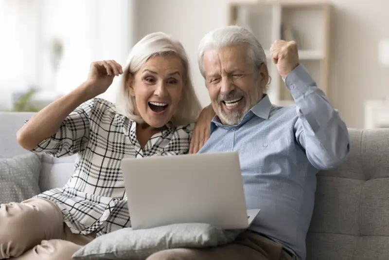 Szczęśliwi seniorzy sprawdzają na laptopie przeliczenie emerytury rocznik 1949 do 1953.