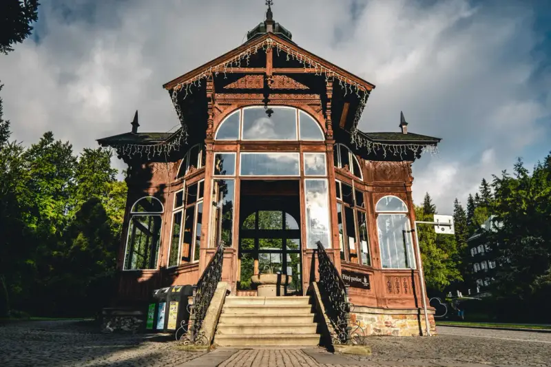 Drewniany pawilon w Karlovej Studance, ozdobiony lampkami, zaprasza do środka. Wspaniała architektura i otoczenie lasu tworzą magiczną atmosferę.