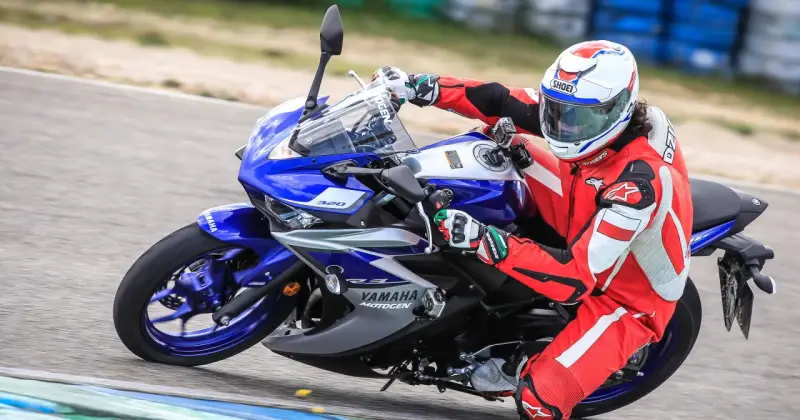 Motocyklista w czerwonym kombinezonie i kasku ściga się na torze na motocyklu Yamaha R3.