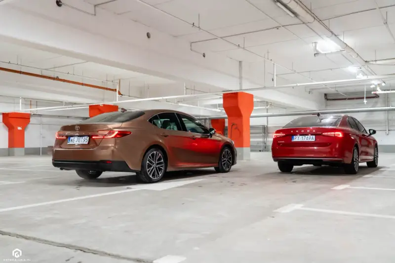 Brązowa Toyota Camry i czerwona Skoda Superb stoją w garażu podziemnym.