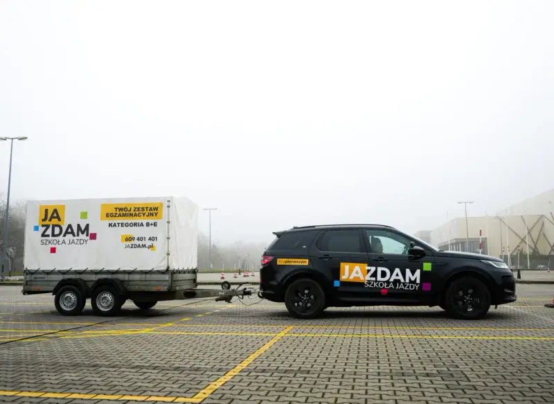 Czarny SUV z przyczepą szkoleniową "JA ZDAM" na placu manewrowym. Zestaw do kategorii B+E gotowy do egzaminu.