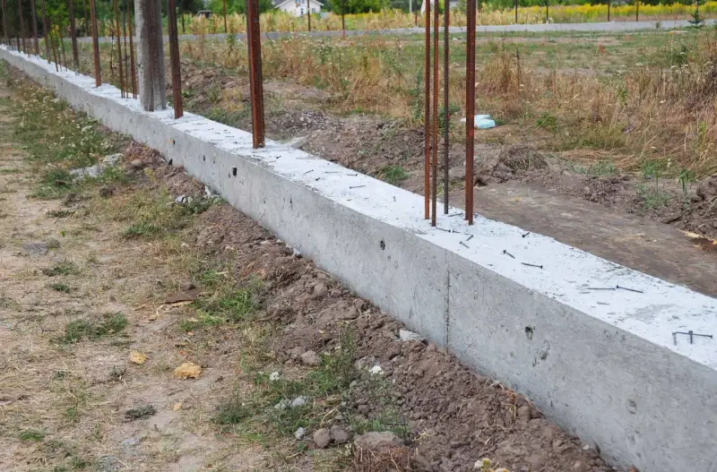 Zbrojony fundament czeka na wylewanie betonu. Widać stalowe pręty wystające z betonowej ławy fundamentowej.