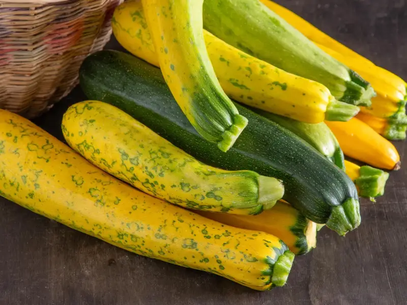 Frische, bunte Zucchini liegen neben einem Korb. Perfekt, um sie roh zu essen und den Sommer zu genießen.