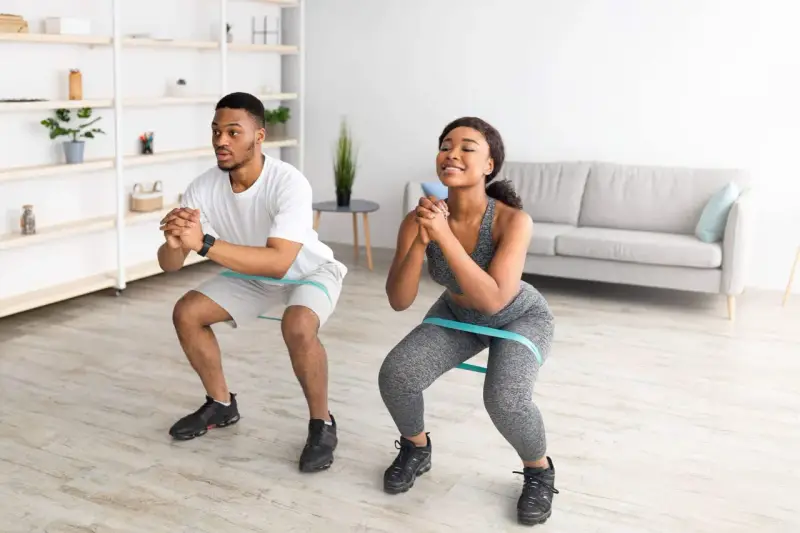 Pareja haciendo sentadillas con bandas elásticas para glúteos en casa.