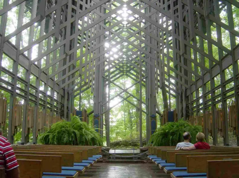 Wnętrze kaplicy w lesie, gdzie architektura organiczna łączy się z naturą. Drewniane ławki, paprocie i światło przenikające przez kratownicę tworzą spokojną atmosferę.