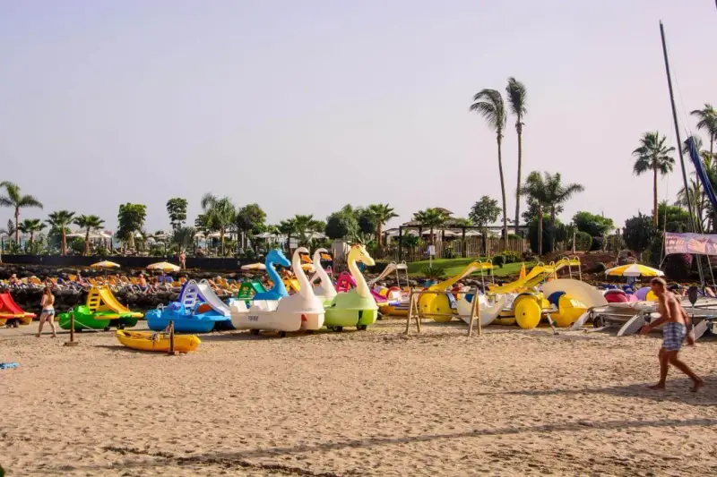 Diversión en Gran Canaria con niños: barcas de pedales con forma de cisne y toboganes esperan en la playa para un día inolvidable.